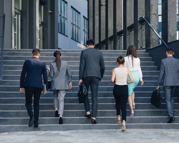  Six businesspeople in formal attire walk up outdoor steps toward a modern office building, representing professionals from an Edible Oil Refinery Plant Manufacturer in India as they head to a corporate meeting.
